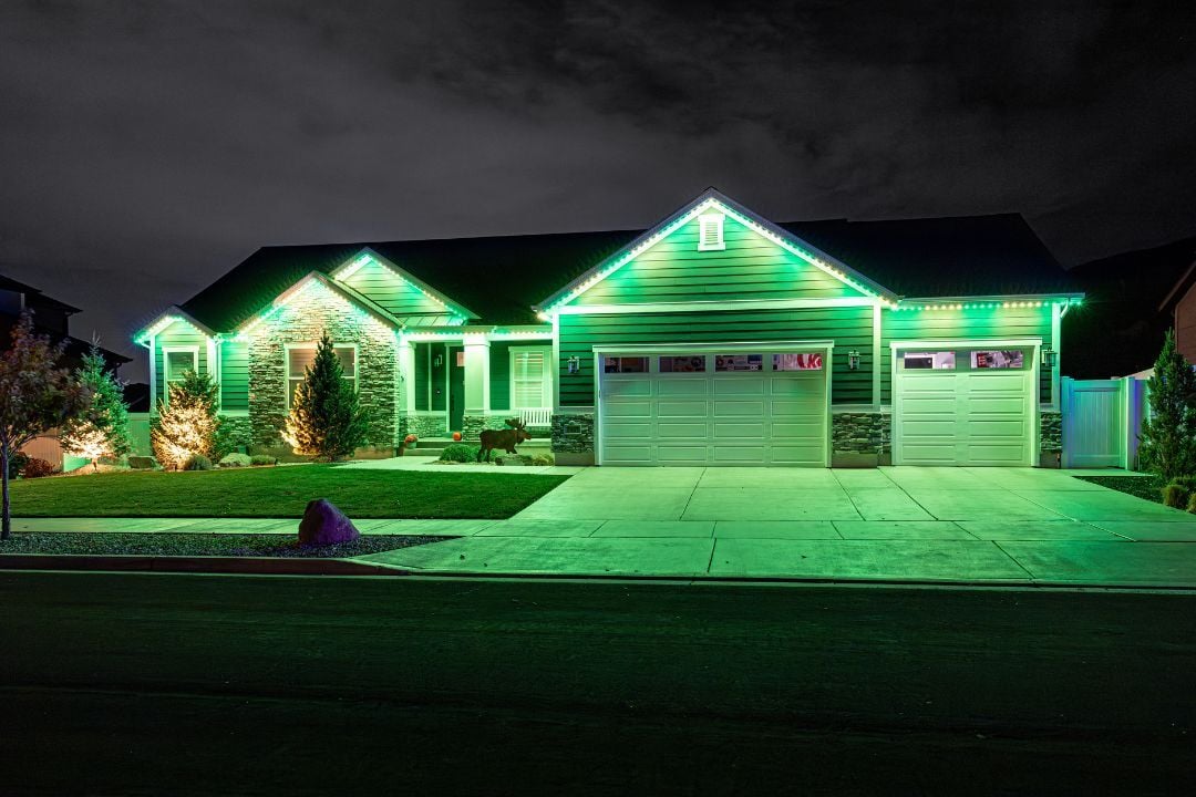 A picture of a home with a Trimlight gold and green pattern with a driveway, and a rock in front.