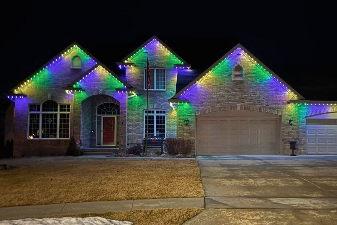 A picture of a home that has 4 peaks and has yellow grass out front with a Trimlight Green, Yellow and Purple lighting pattern.