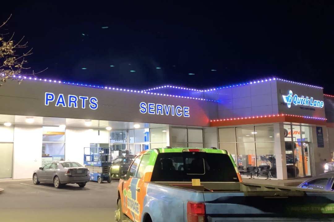 A Quicklane car parts store that has blue and white Trimlight and has a green and orange truck in frame.